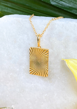 Load image into Gallery viewer, Gold Minerva Pendant on white slab with leaves and flowers.