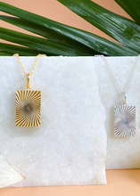 Load image into Gallery viewer, Gold and Silver Minerva Pendants on white marble slab with leaves and flowers.