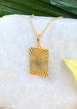 Load image into Gallery viewer, Gold Minerva Pendant on white slab with leaves and flowers. 
