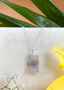 Silver Minerva Pendant on white marble slab with leaves and flowers.