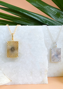 Gold and Silver Minerva Pendants on white marble slab with leaves and flowers.