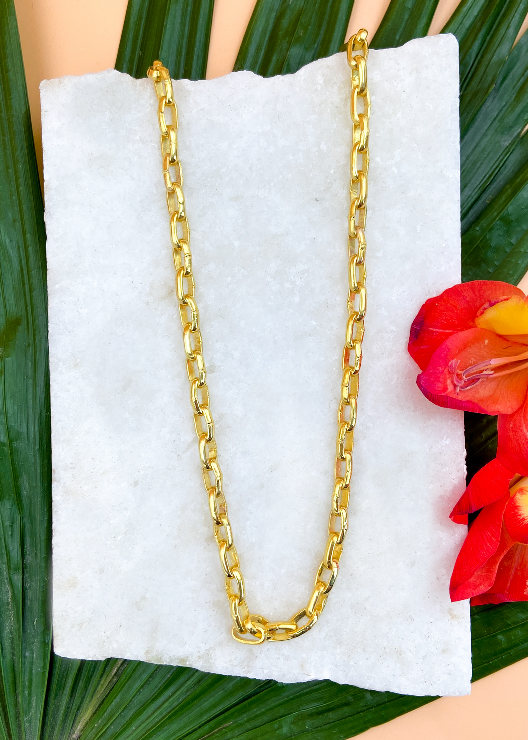 Catena necklace in gold on marble slab with leaves and flowers