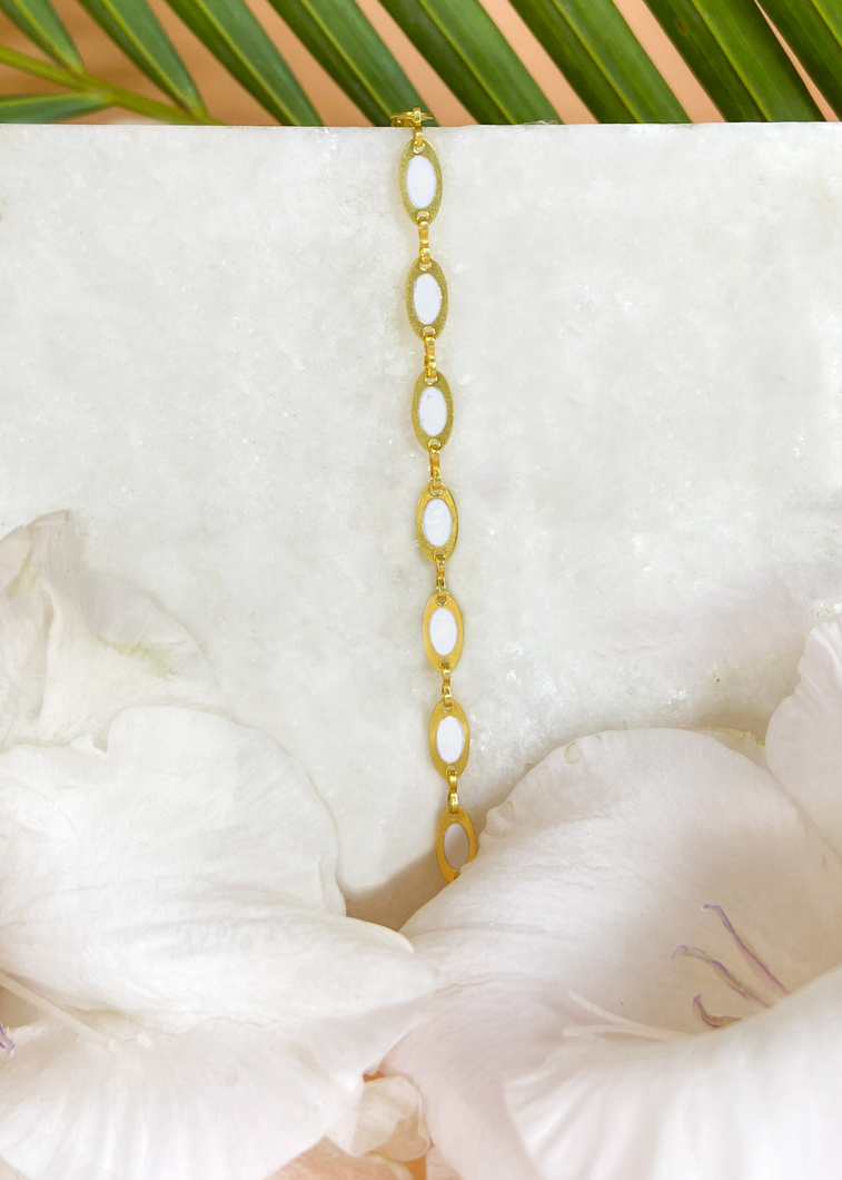 Delicate Tia bracelet on marble slab with white flowers at the side and palm leaf at the back