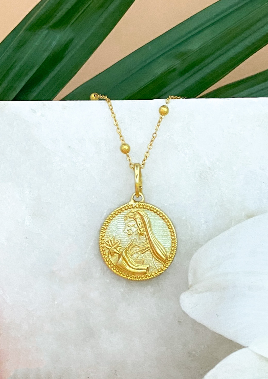 Golden Modern Maharani Pendant on white marble slab with leaves and flowers