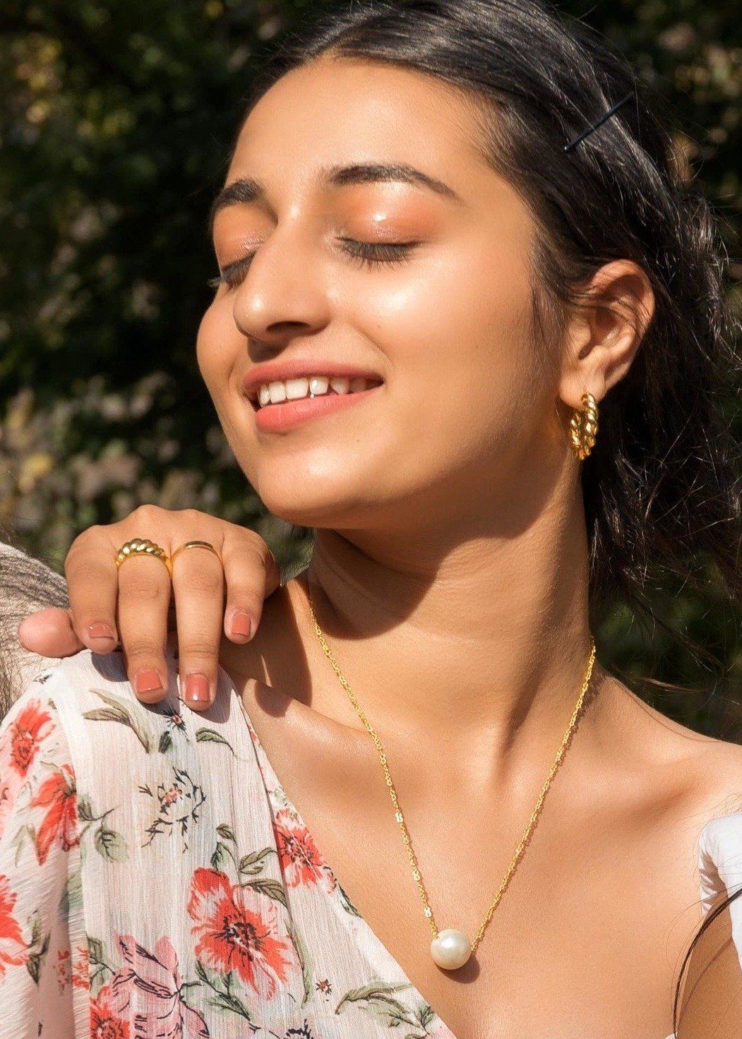 Model sitting outside thin the sunlight wearing Amora Pearl Necklace and Twirl Earrings.  